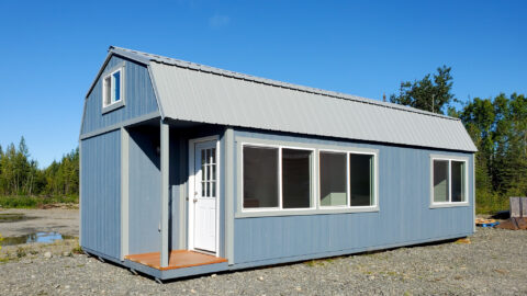 Exterior view of the Black Bear Modular showcasing light blue siding, a gambrel roof, white trim, a small porch with a white door, and large windows.