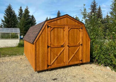 Cedar-stained Barn with gambrel roof, double barn doors, and brown shingles, surrounded by greenery.