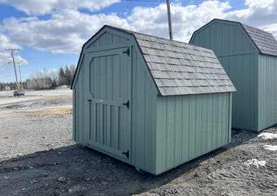 A compact green Barn by Northwood Buildings with a gambrel roof, single door, and black shingle roofing.